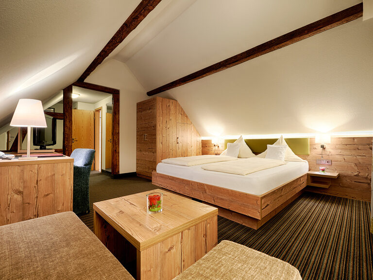 Ein großes Doppelbett in einem Hotelzimmer, welches von Lichtern beleuchtet wird, erstrahlt in gemütlicher Atmosphäre.