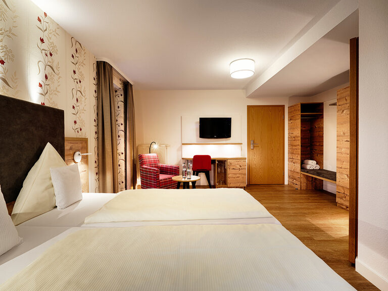 Ein ggroßzügiges Doppelbett mit weißer Bettwäsche steht in einem geräumigen Hotelzimmer.