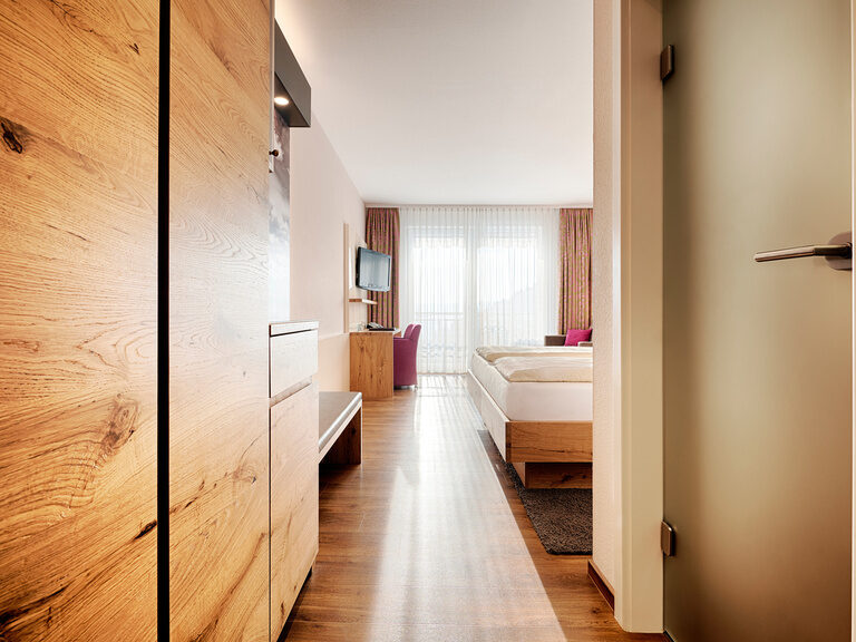 Ein Zimmerflur mit Boden in Holzdesign und Schränken, einer Türe zum Badezimmer und Blick in den Wohnbereich.