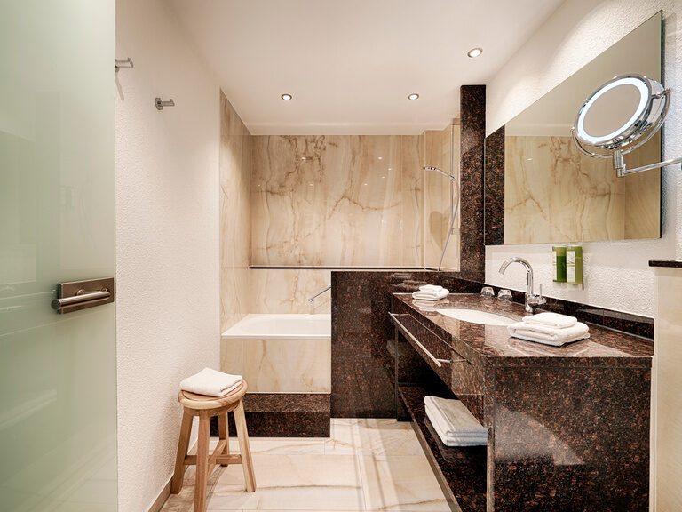 Ein, in Marmoroptik ausgestattetes, Badezimmer mit großer Badewanne, Waschbecken, Toiletten und Handtuchwärmer.